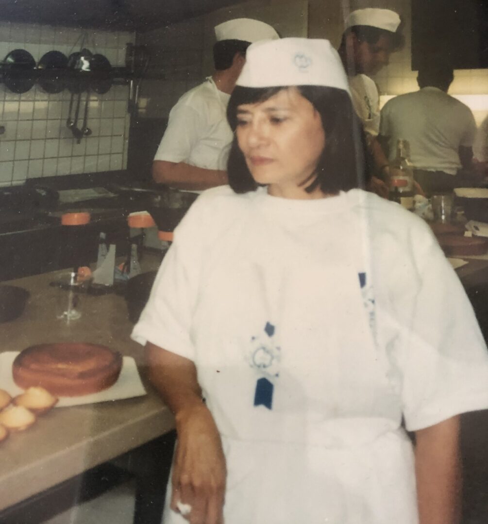 A woman in white shirt and hat standing next to counter.