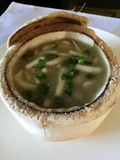 A bowl of coconut soup with green onions, served in a hollowed-out coconut shell.