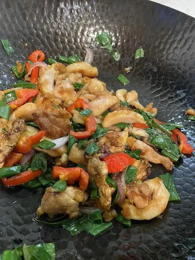 Stir-fried shrimp with red peppers, onions, and green herbs in a black wok.