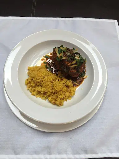 A plate of rice with a garnished, grilled chicken thigh, served on a white plate on a dark tablecloth.