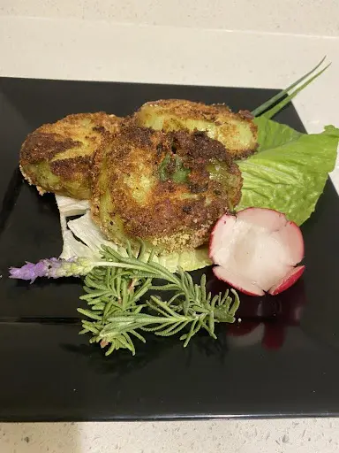 Plate of fried green tomatoes garnished with herbs and a radish on a black rectangular plate.