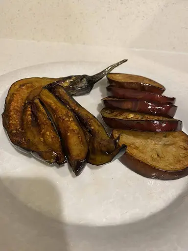 Sliced and roasted eggplant pieces on a white plate, showing both charred and tender textures.