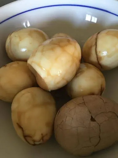 A bowl containing several tea-stained eggs with one showing cracks on its shell.